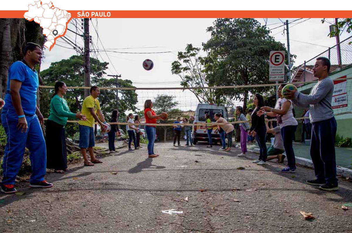 Adolescentes e adultos trocam passes em dupla em quadra de vôlei improvisada em uma rua. Acima da imagem, mapa do Brasil com marcação que destaca cidade de São Paulo.