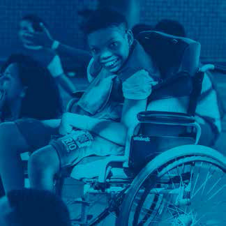 menino em cadeira de rodas acena e sorri.