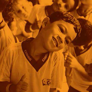 menino com a cabeça apoiada em seu no ombro esquerdo sorri. Ao fundo outros estudantes fazem o mesmo movimento.